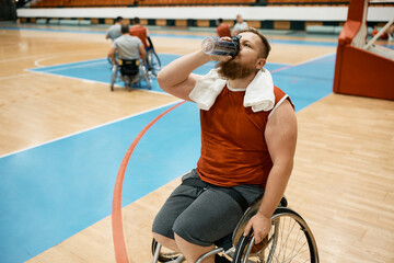 Thirsty wheelchair-bound basketball player drinks water after sports training.