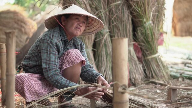 Asia life old femen  grandmother working in outdoor.
Old lady elderly serious living in the countryside of life rural people in thailand . Weaving material grass roof groof bamboo mak