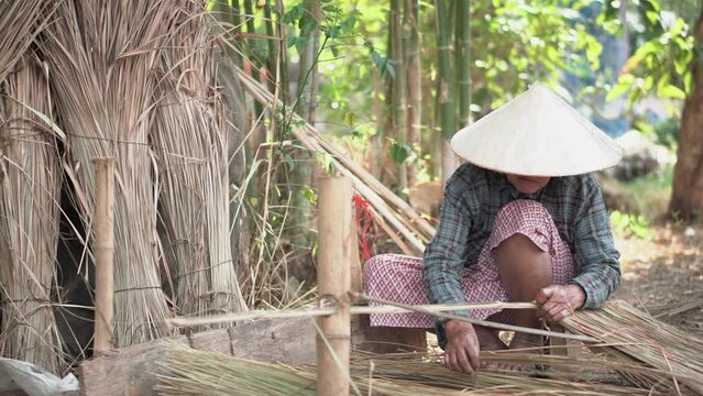 Asia life old femen  grandmother working in outdoor.
Old lady elderly serious living in the countryside of life rural people in thailand . Weaving material grass roof groof bamboo mak