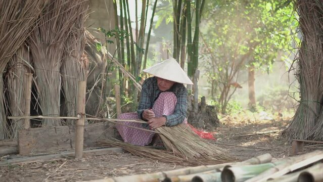 Asia life old femen  grandmother working in outdoor.
Old lady elderly serious living in the countryside of life rural people in thailand . Weaving material grass roof groof bamboo mak