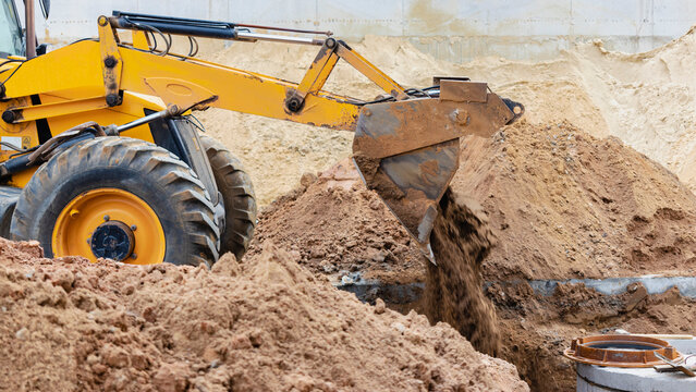 The excavator backfills the pit with the front bucket. Moves soil around the construction site. Close-up. Heavy construction equipment.