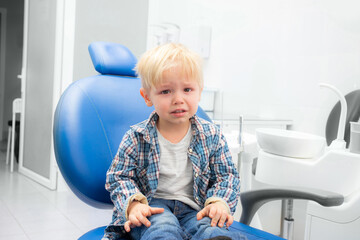 little blond boy is crying in the dentist's chair. primary teeth treatment