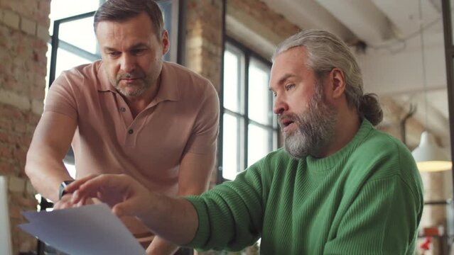 Two middle aged businessmen discussing documents in office during workday