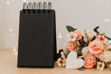 notebook with black sheets with copy space, a bouquet of flowers and a white heart