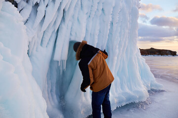 A man studies huge icicles on the rocks. Winter trip on the frozen lake Baikal. 