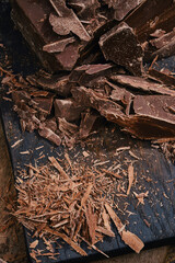 Composition of bars and pieces dark chocolate with chocolate chips on a wooden cutting board. Сrushed dark chocolate. Chipped dark chocolate pattern. Shallow depth of field.