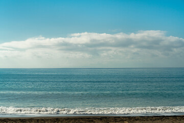Front view of a sand beach with waves blue sea and blue sky and white clouds