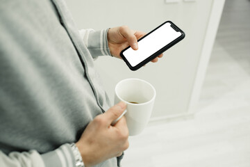 Phone on hand, young man is holding the phone in his hand, he has a coffee mug in his other hand, free space on the phone. Selective focus, noise effect.