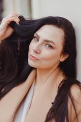 Fototapeta premium Young brunette woman in beige winter coat stands alone on the street