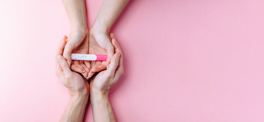 Pregnancy test kit. Female hand hold positive pregnant test with silk ribbon on pink banner...