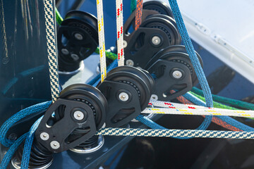 Part of the mast and hull of a sailing yacht, with multi-colored ropes, rollers and hinges for...