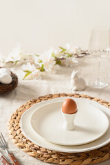 Fototapeta na wymiar Happy Easter morning, festive dinner with egg, bunny, fresh flowers on white linen tablecloth. Vertical format. Close up.