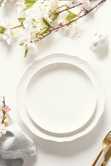 Easter festive dinner with golden eggs, festive tableware and flowers on white background. Top view. Festive tablescapes. Vertical format.