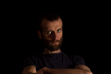 A serious man on a dark background in a dark T-shirt holds his hands in front of him. place for text