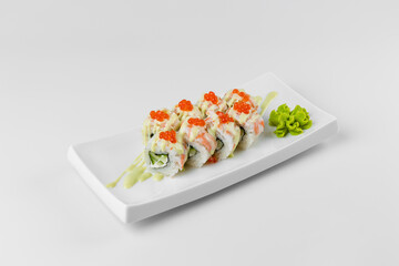 Sushi roll with red caviar, rice and cucumber on a white plate with a white background. Wasabi and pink ginger.