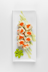 Sushi roll with red caviar, rice and cucumber on a white plate with a white background. Wasabi and pink ginger.