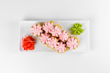 Japanese tempura hot sushi roll on white plate and background. Sushi pieces with salmon, eel, cucumber, cream cheese, avocado wrapped in rice with crunchy seaweed on top with greens