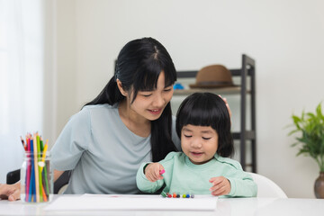 Happy asian boy painting with crayon and colored pencil with his mother in living room at home. Mom teaching son how to painting with crayon color on book or doing homework. family concept.