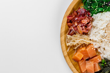 Poke with rice, sesame seeds, cucumbers, fish tomatoes, tangerines, peas, cabbage and sauce. Wooden plate on a white background.