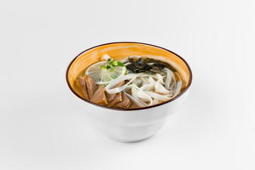 Hot soup with pork pieces, noodles, green onions, lime and nori seaweed. Deep plate on a white background.