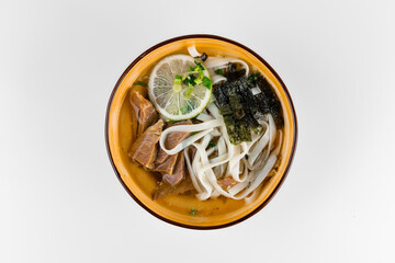 Hot soup with pork pieces, noodles, green onions, lime and nori seaweed. Deep plate on a white background.