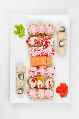 Set of different sushi rolls with rice, fish, cucumbers, wasabi, ginger, caviar and sesame. Large white plate on a white background. Lots of sushi in one dish.
