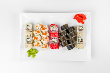 Set of different sushi rolls with rice, fish, cucumbers, wasabi, ginger, caviar and sesame. Large white plate on a white background. Lots of sushi in one dish.