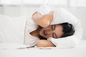 Asian woman Lie face down and put a pillow over her head because the side of the house makes a loud...