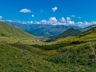 Naklejka na ściany i meble A panoramic view on the alpine pasture of a valley near the village in Roshka in the Greater Caucasus Mountain Range in Georgia, Kazbegi Region. Landscape with green hills. Wanderlust.