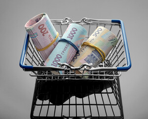 Shopping cart with hryvnia banknotes on a gray glossy background. Waste of money in the store. Concept of finance, sales, investment, marketing concept