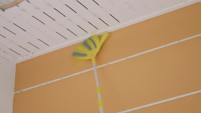 Cleaning ceiling cobwebs with an extension broomstick or plastic brush.