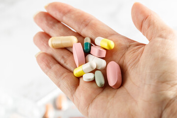 Aged female hand with pills on light background.