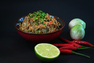 A bowl of traditional northeastern style spicy mash eggplant and mackerel dipping paste sauce topped with fresh green spring onion with lemon and fresh red chili in isolated black background 