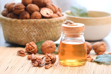 Close up of a bottle of walnut oil with kernels and its shell in a pannier and green leaves in background 
