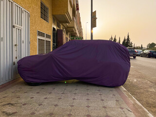Unrecognizable car covered with protective cloth outdoors