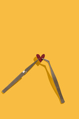 Red heart and tweezers on a yellow background. Valentine day concept. Study test and love experiment. Broken heart idea. Flat lay with copy space.