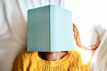 Ive always got my head stuck in the books. Shot of an unrecognizable woman lying with a book over...