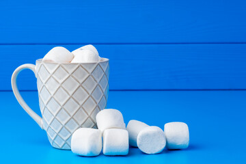 Cup of hot cocoa drink with marshmallows on blue background