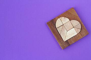 Wooden puzzle details in wooden heart-shaped box on purple background