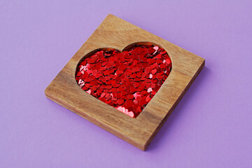 Fototapeta na wymiar Wooden heart-shaped box with red sequins in form of hearts on purple background