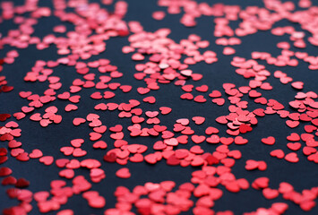 Scattered random red sequins in form of hearts on black textured background