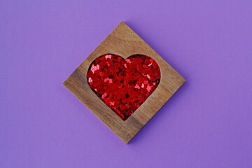 Wooden heart-shaped box with red sequins in form of hearts on purple background