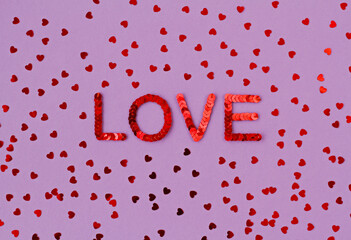 Inscription of "Love" embroidered with red sequins on purple background with scattered random sequins in form of hearts