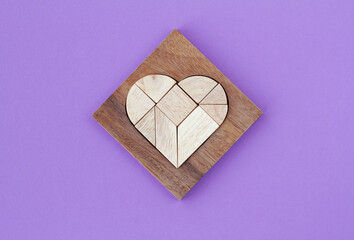 Wooden puzzle details in wooden heart-shaped box on purple background