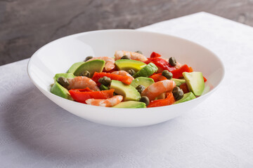 A view of a plate of salad with avocado, pepper, shrimps, capers on white plate. Mediterranean cuisine. Isometric style.