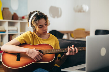 teenager boy playing acoustic guitar at home. he has online lesson