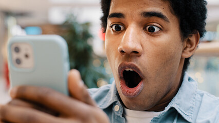 African american guy surprised by message received wins online bets looking at mobile phone opens...