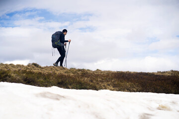 The traveler is engaged in extreme sports, climbs to the top of a snow-covered mountain with tourist equipment in backpacks and trekking poles. A young man is hiking alone in the winter wild nature.