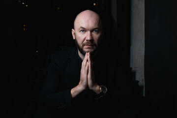 Bald and bearded man is expensively dressed. Man says a prayer