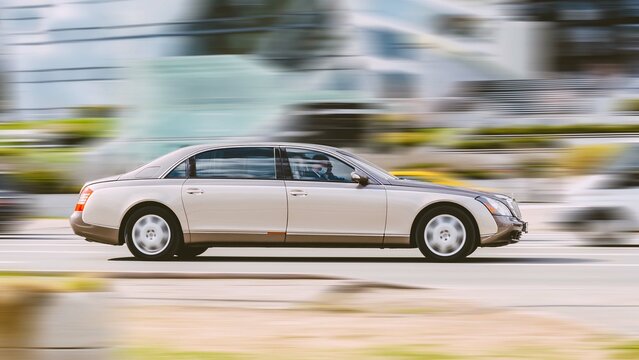 Maybach 62 S limousine is driving along the street in city with blurred background. Side view rolling shot with premium business car in motion